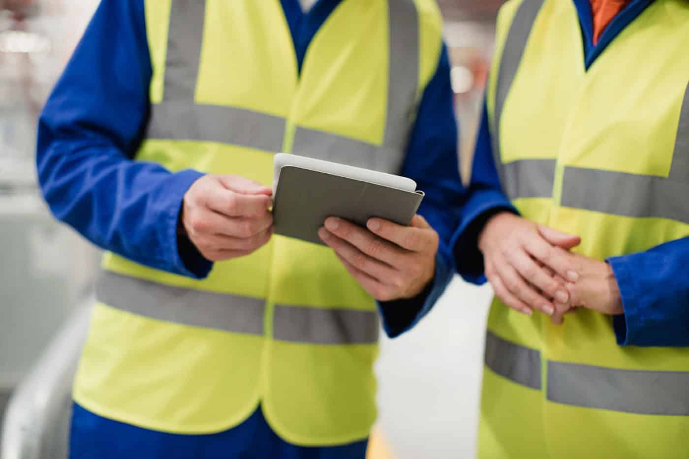 two employees in hi-vis vests discussing notes - only torso, no heads